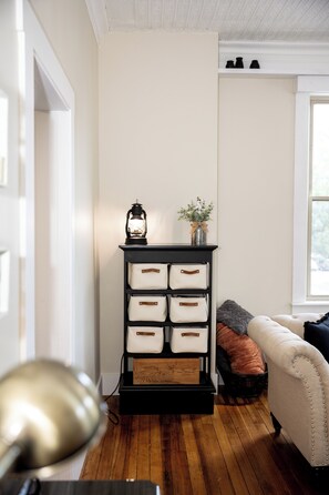 A room with a wooden floor, a black storage unit with drawers, a lamp, a sofa, and a window. - The Loft on the Square (Highland)