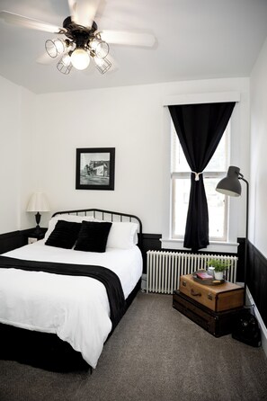 A bedroom with a bed, a radiator, a suitcase, a lamp, a picture on the wall, and a window with curtains. - The Loft on the Square (Highland)