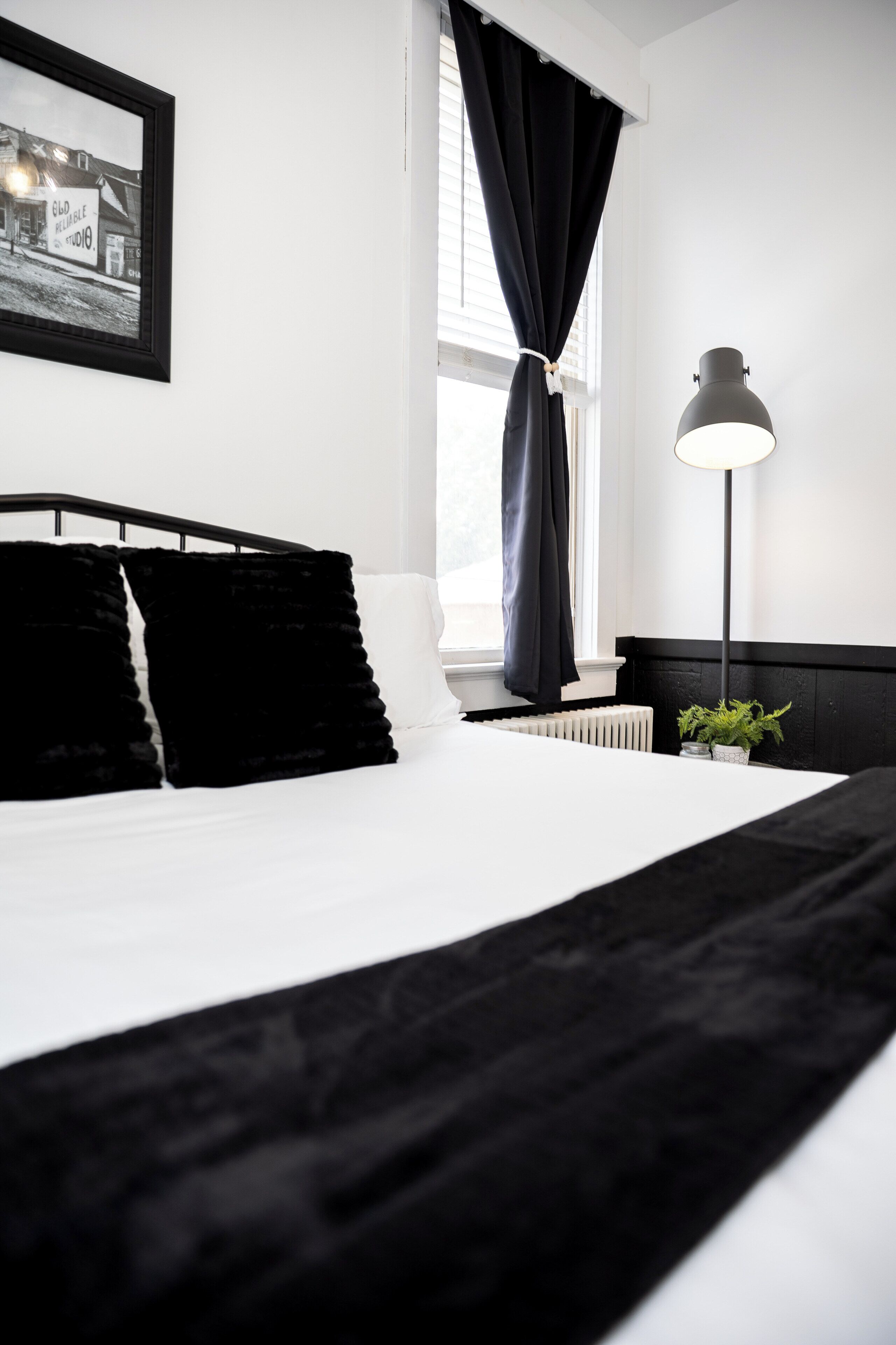 Een net opgemaakt bed met zwart-wit beddengoed, een bedlampje en een ingelijst schilderij aan de muur.