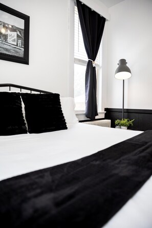 A neatly made bed with black and white bedding, a bedside lamp, and a framed picture on the wall. - The Loft on the Square (Highland)