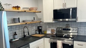 Una cucina moderna con mobili bianchi, un frigorifero in acciaio inossidabile, un forno a microonde, un forno e una macchina da caffè.