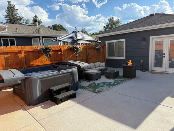 A backyard with a hot tub, outdoor seating, a wooden fence, and a house.