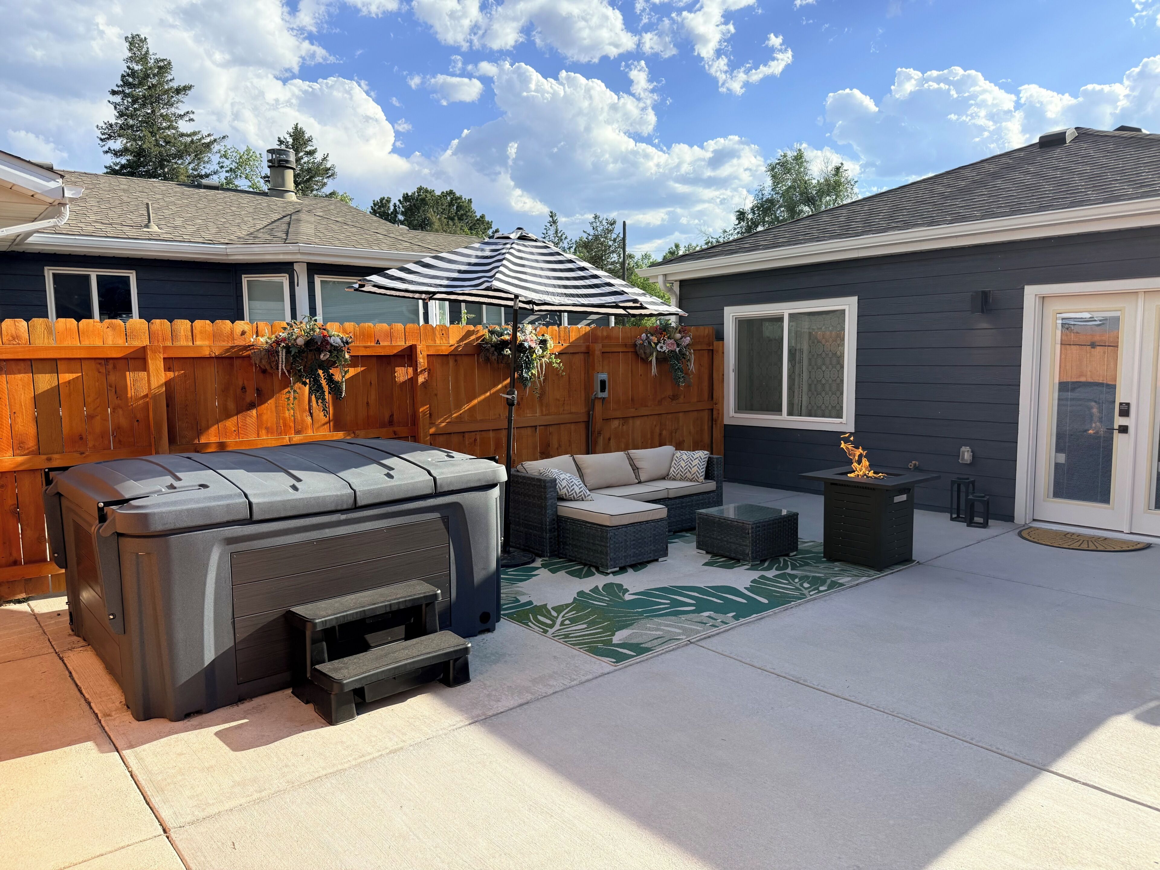 Een achtertuin met een jacuzzi, tuinmeubilair, een houten omheining en een overdekt terras.