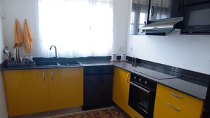Une cuisine avec des meubles de couleur jaune, un plan de travail noir, un évier, une cuisinière et un four à micro-ondes.