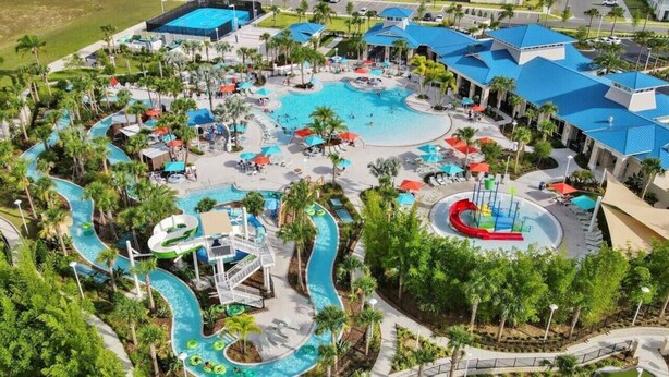 Vista aérea de un complejo turístico con una gran piscina central, varias toboganes acuáticos y palmeras circundantes.