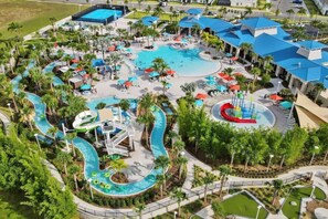 An aerial view of a resort with a large central pool, multiple water slides, and surrounding palm trees.