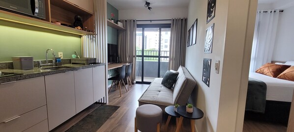 A compact hotel room with a kitchenette, a sofa, a small table, and a bed.