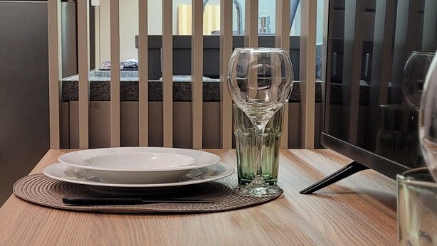 Ein Esstisch ist mit Tellern, Besteck und einem Glas gedeckt.