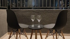 Ein moderner Essbereich mit einem runden Tisch, zwei Stühlen, einem Weinglas und Blick auf die beleuchtete Stadt bei Nacht.