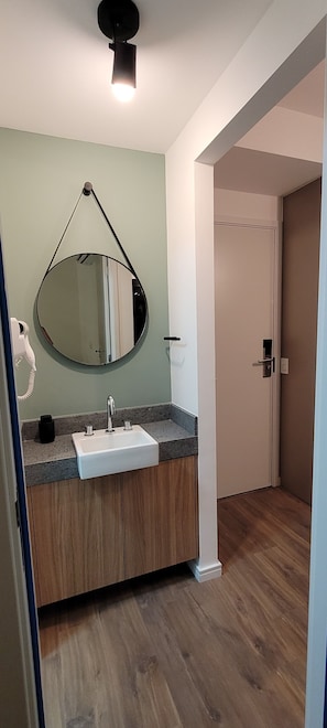 Ein Badezimmer mit einem weißen Waschbecken, einem runden Spiegel und Holzschränken.