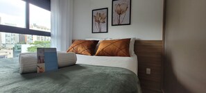 Une chambre d’hôtel avec un lit, des oreillers, une table de chevet et une fenêtre donnant sur la ville.