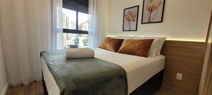 A hotel room with a bed, a window with curtains, and two framed pictures on the wall.
