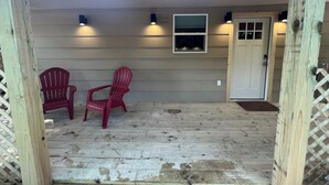 A wooden porch with two red Adirondack chairs, a small window, and a door. - Cozy farmhouse cabin near Kilgore and Longview (Longview)