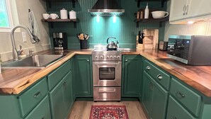A kitchen with green cabinets, a stainless steel stove, a microwave, and a red rug. - Cozy farmhouse cabin near Kilgore and Longview (Longview)