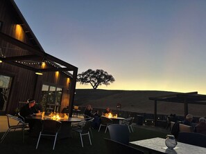 An outdoor dining area with tables and chairs, a fire feature, and a view of the landscape.