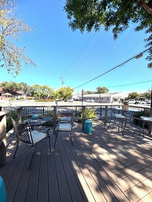 An outdoor deck with tables and chairs, surrounded by trees and a clear sky.