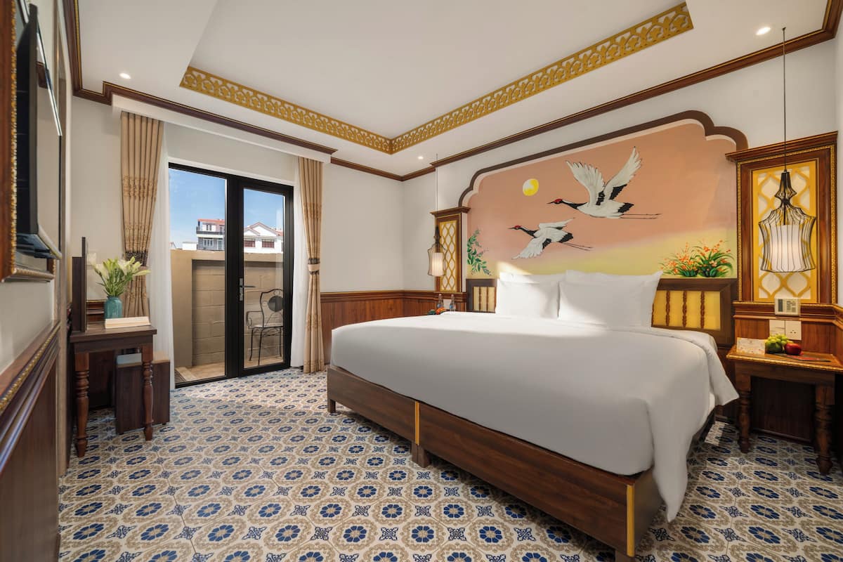 A hotel room with a large bed, a wooden headboard, a mural of birds, a view through a glass door, and patterned floor tiles.