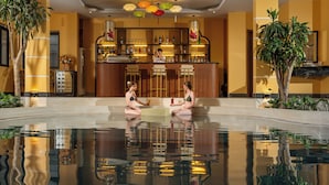 Zona de bar con una piscina al frente, una recepción y una barra con botellas y vasos.