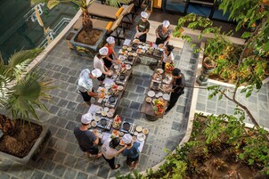 Un restaurante en la azotea con varias mesas y sillas, rodeado de plantas en macetas y una piscina.