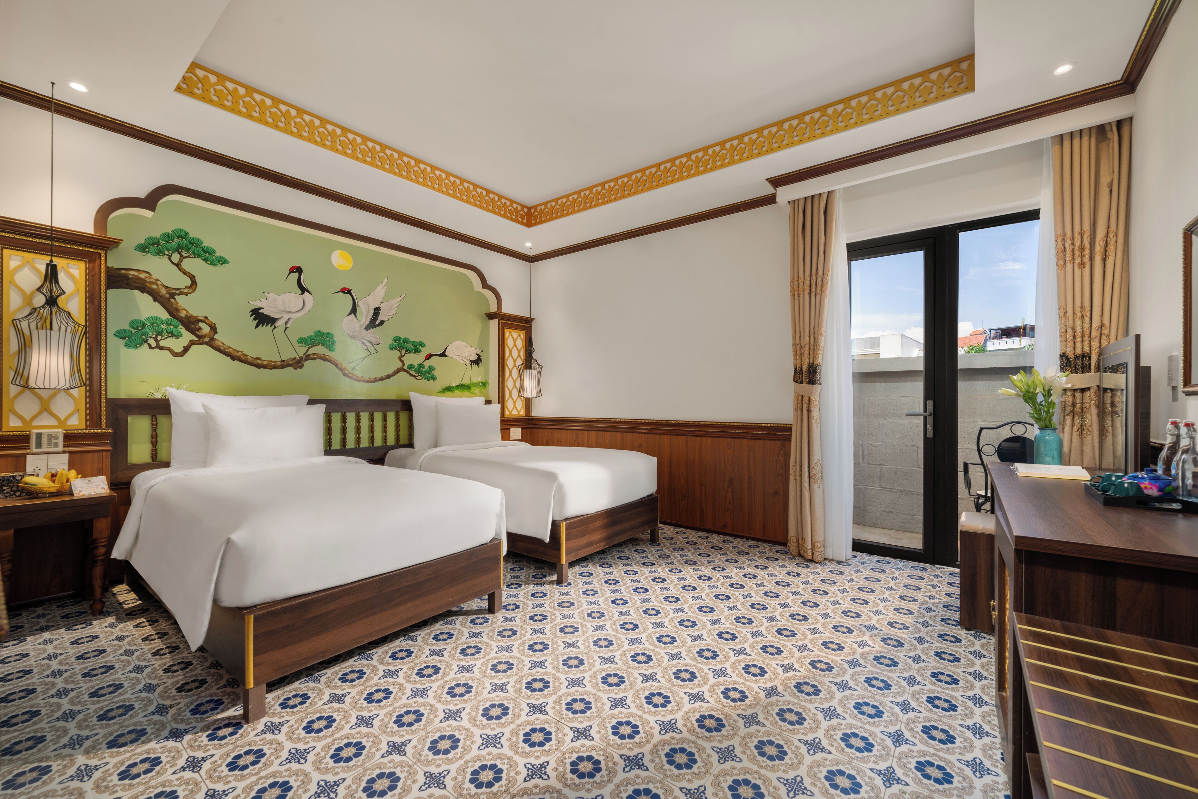 Habitación de hotel con dos camas, un mural grande, piso estampado y un escritorio con un florero.