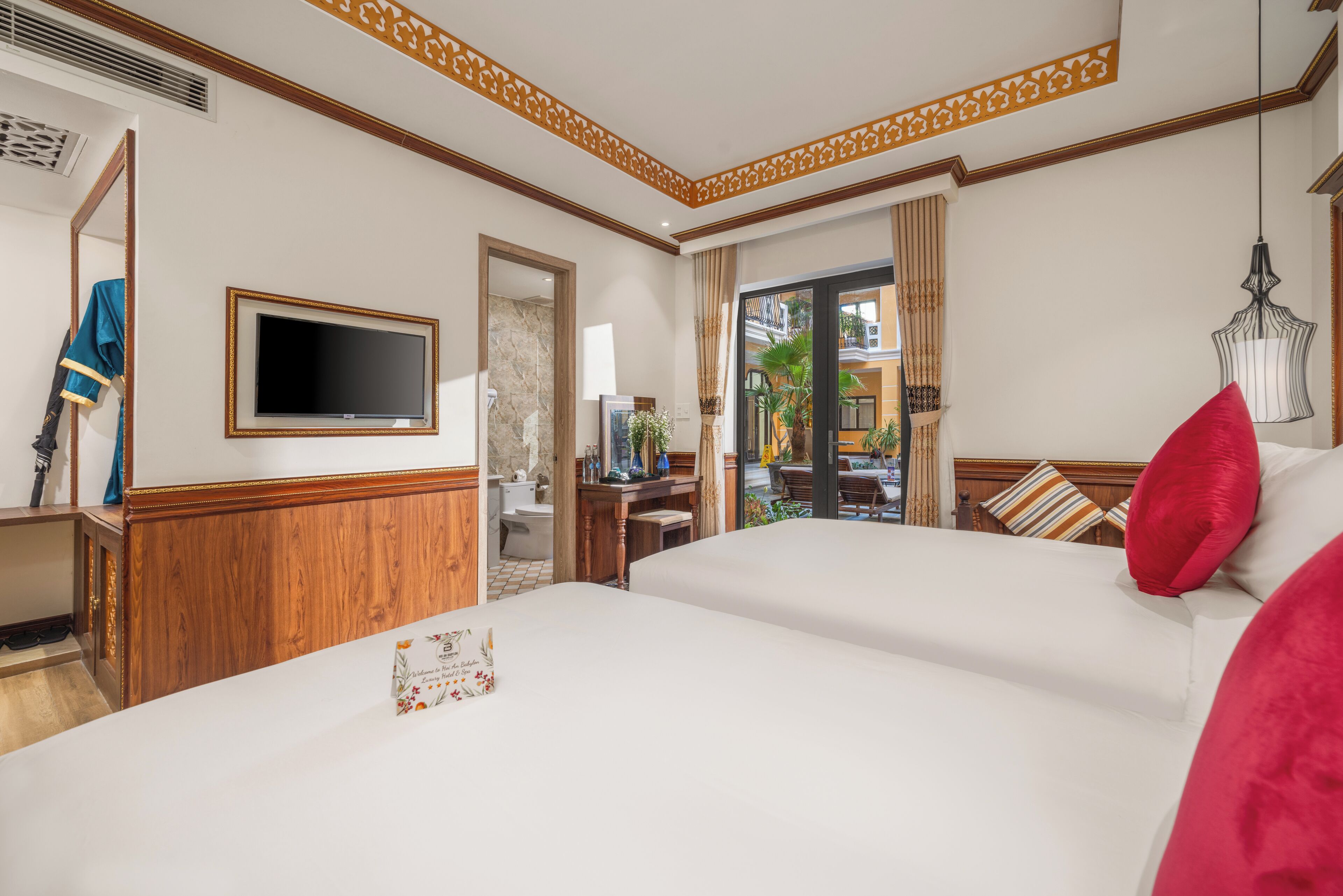 A hotel room with a large bed, a television, a wooden dresser, and a view of the outside balcony.