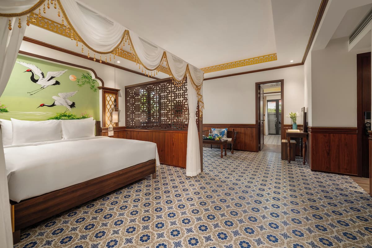 A spacious bedroom with a large bed, a wooden headboard, a decorative screen, and a mural of birds.