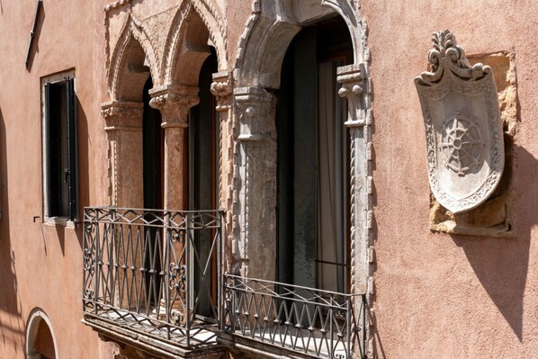 A building facade with a wrought iron balcony, arched windows, and a coat of arms.