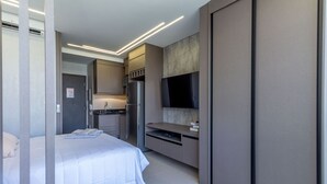 A modern hotel room with a bed, a kitchenette, and a flat-screen TV mounted on the wall. - Apartamento/sp/perdizes/allianz/wi-fi 500mb/rooftop/piscina/vaga (Perdizes São Paulo)