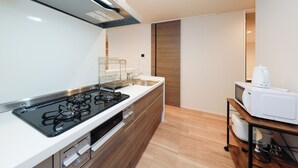A modern kitchen with a gas stove, microwave, and a coffee maker on a wooden table. - La Terrasse Higashikomagata by Tranova (Tokyo)