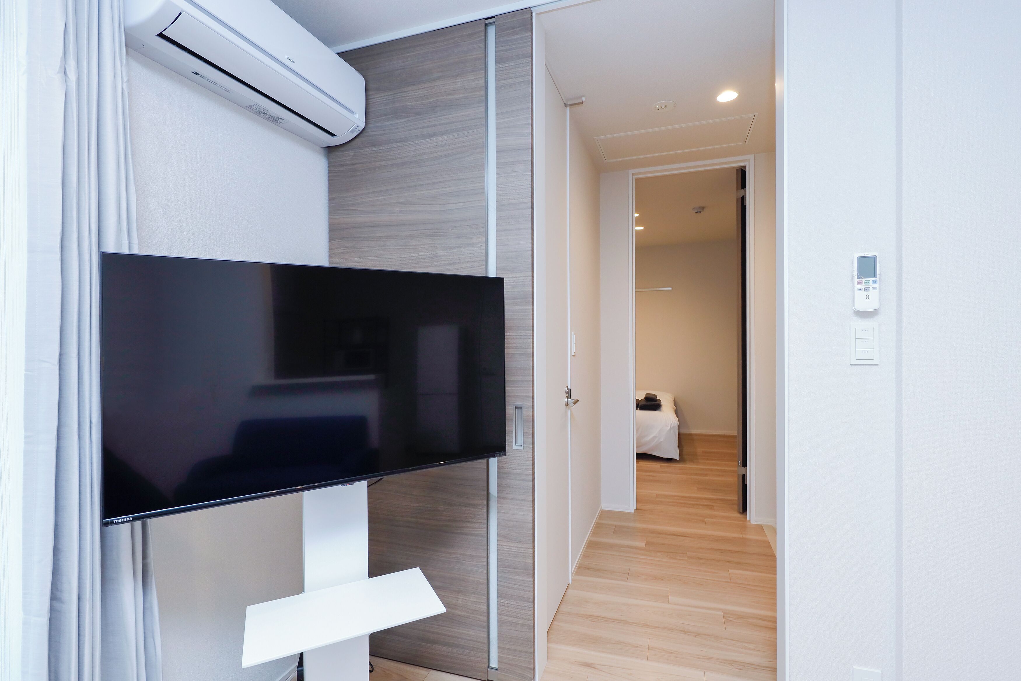 A modern hotel room with a flat-screen TV, sliding doors, a wooden floor, and a wall-mounted air conditioner.