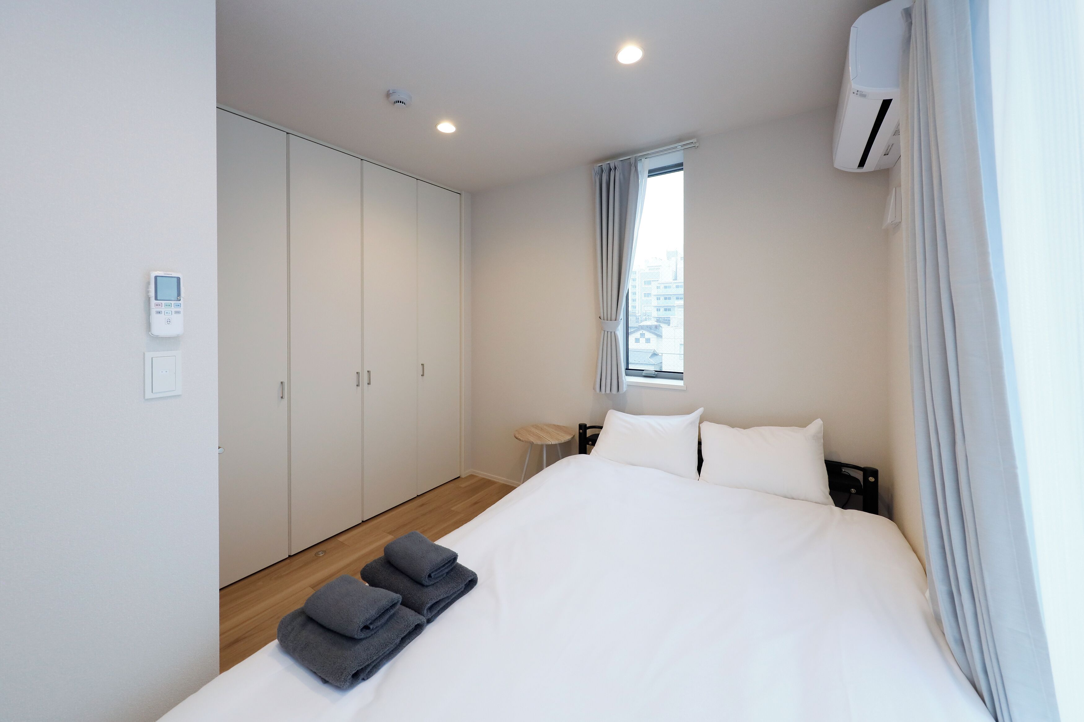 Een moderne hotelkamer met een groot bed, een kledingkast, een klein tafeltje en een airconditioning.