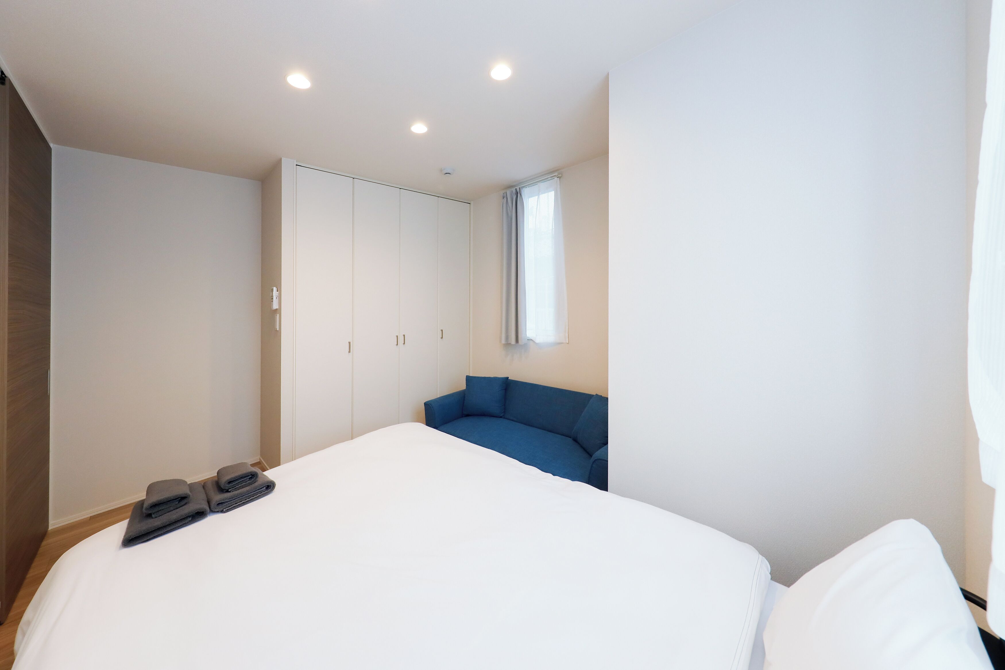 A bedroom with a bed, a blue sofa, a wardrobe, and a window.