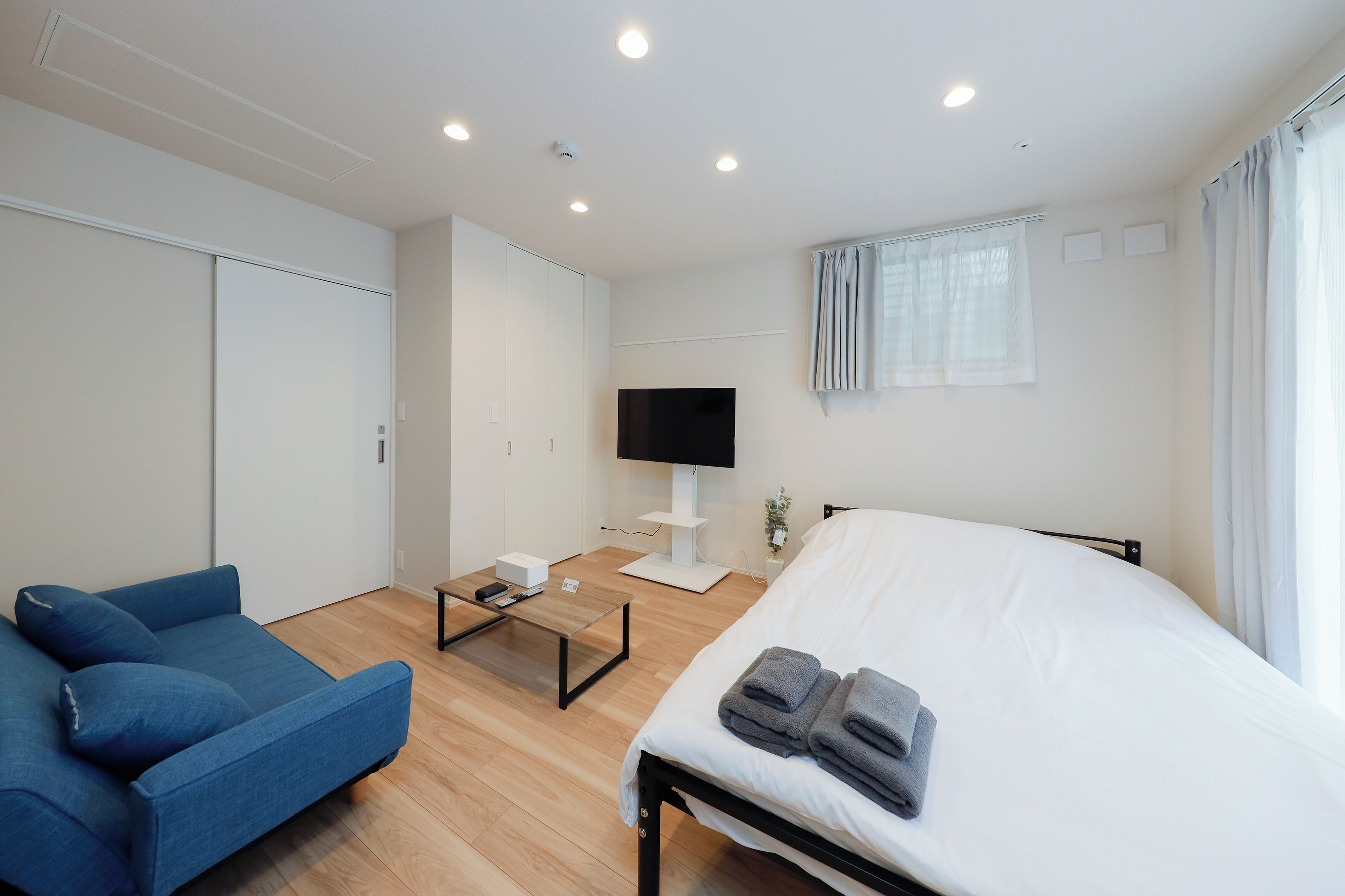A modern hotel room with a bed, a blue sofa, a TV, and a desk with a computer.