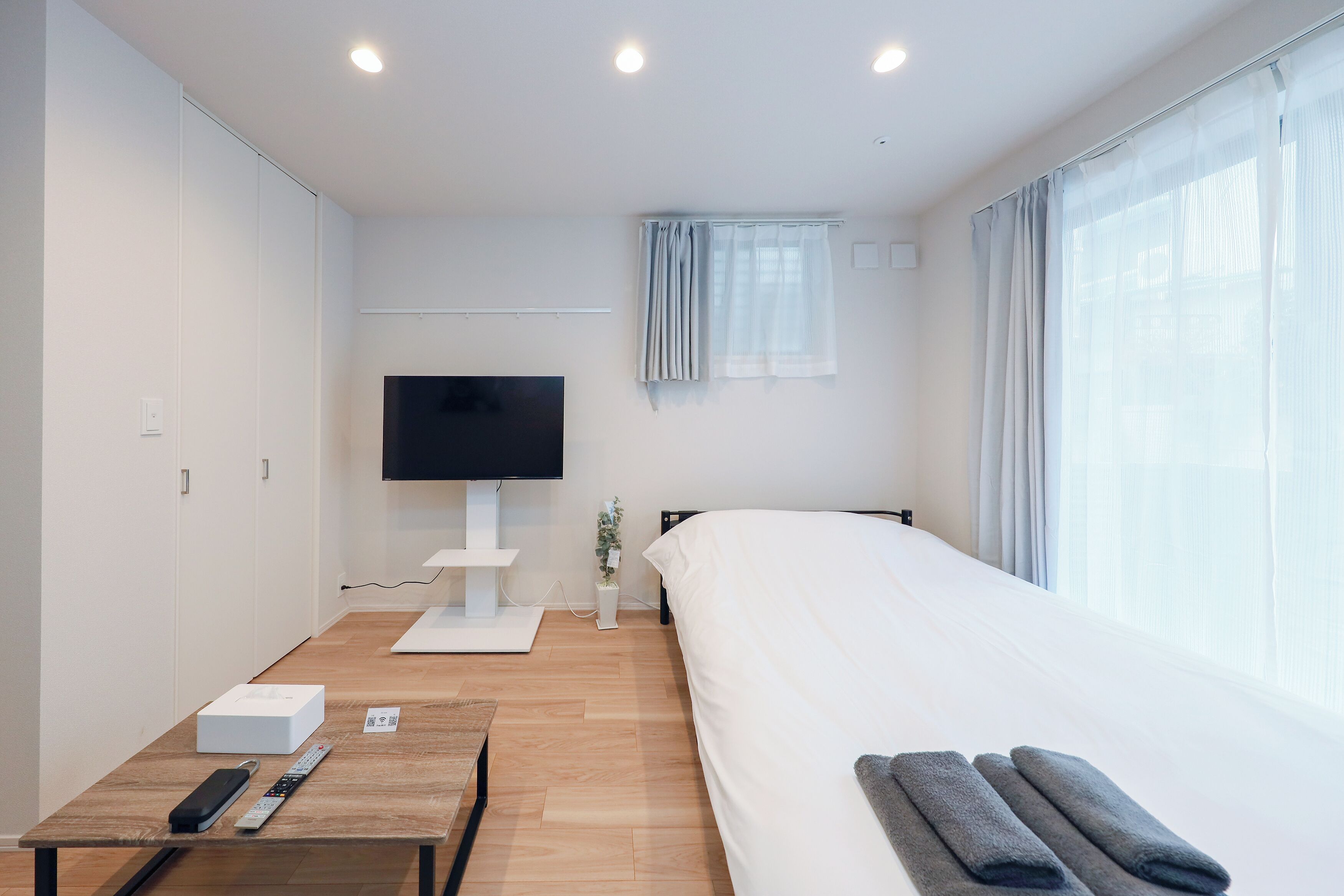 A modern hotel room with a bed, a TV, a desk, and a window with curtains.