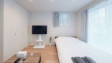 A modern hotel room with a bed, a TV, a desk, and a window with curtains.