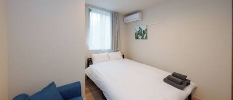 A bedroom with a bed, a window with curtains, an air conditioning unit, and a blue sofa.