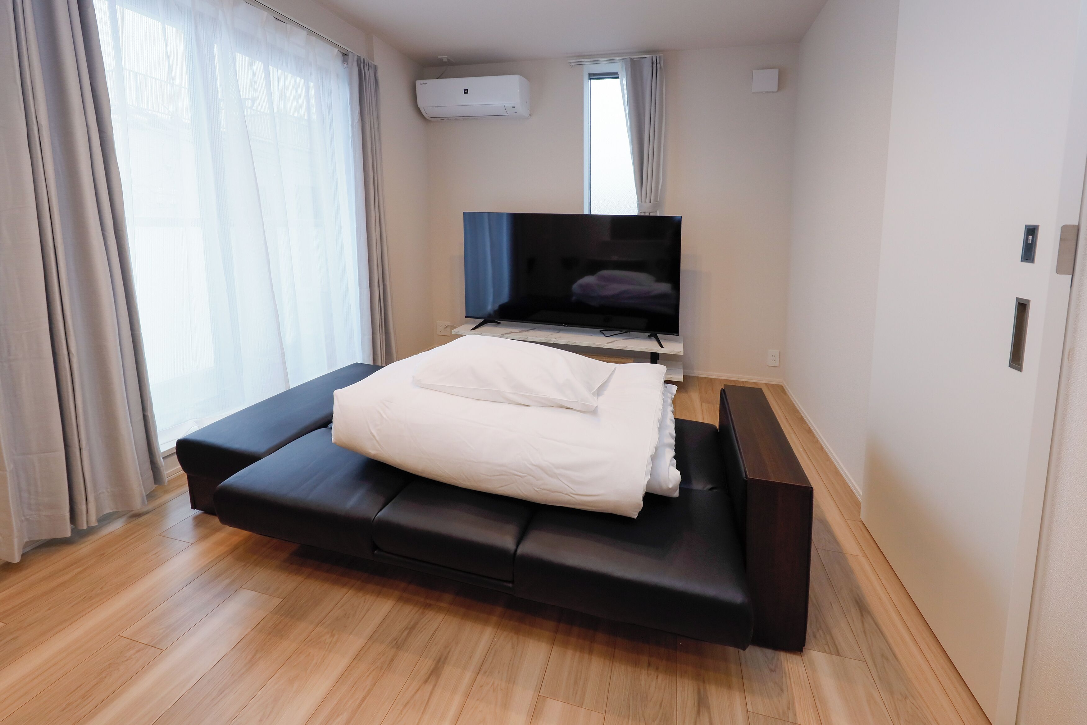 Un dormitorio moderno con cama, televisor de pantalla plana y ventana con cortinas.