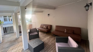 A covered outdoor seating area with two sofas and two chairs, a wooden deck, and a white ceiling.