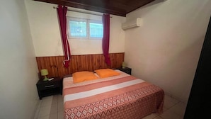 A bedroom with a wooden headboard, a bed with patterned bedding, two bedside tables with lamps, and a window with curtains.