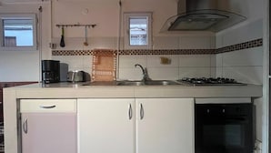 A compact kitchen with white cabinets, a gas stove, a built-in oven, a coffee maker, and a window above the sink.