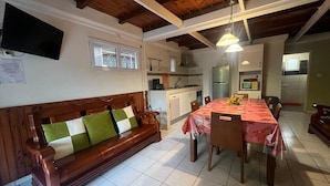 A cozy living area with a wooden sofa, a dining table with chairs, and a kitchen in the background.