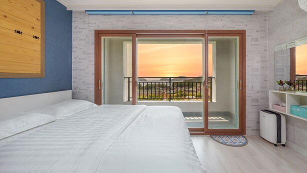 Ein Hotelzimmer mit Bett, einem Balkon mit Sonnenuntergangsblick und einer kleinen Küchenzeile.