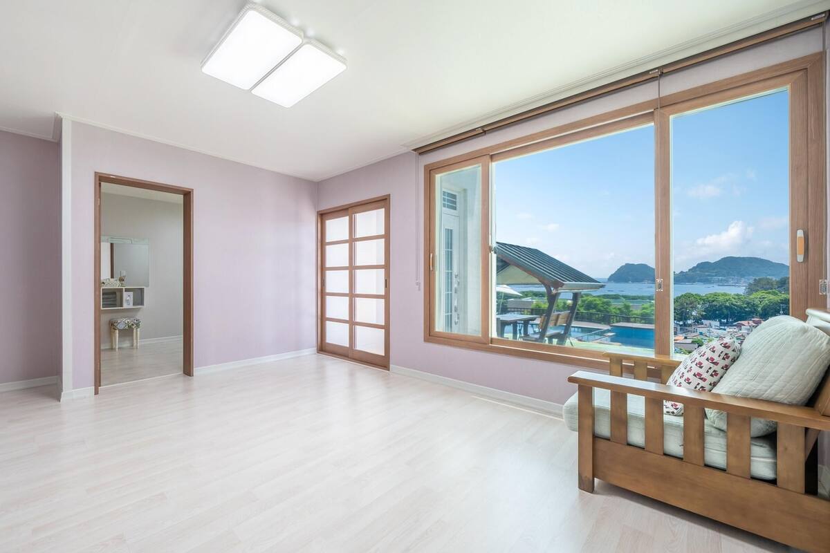 A spacious room with a large window, a wooden bench, and a door leading to another room.