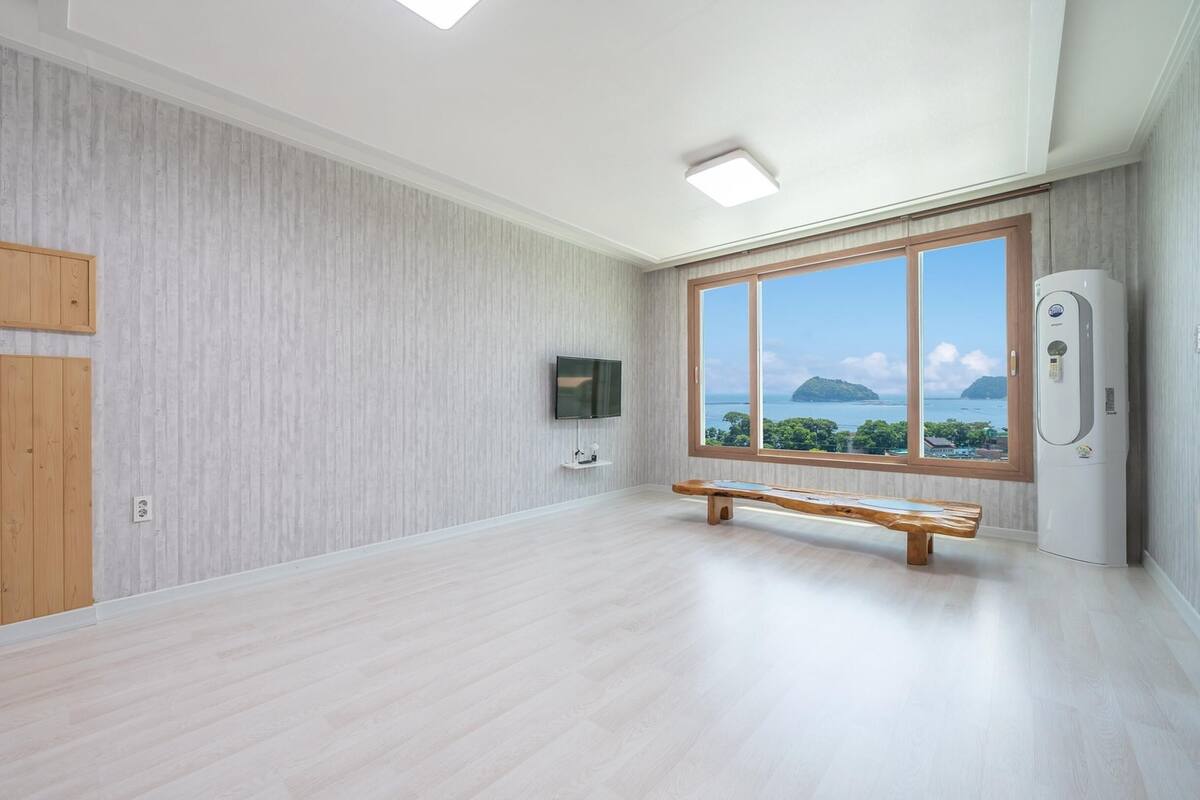 A spacious room with a large window offering a view of the sea and a distant island.
