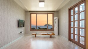Ein Zimmer mit einer hölzernen Bank, einem an der Wand montierten Fernseher und einem großen Fenster mit Blick auf das Meer und einen Berg.