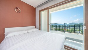 A hotel room with a large bed, a view of a balcony with a railing, and a door leading to the balcony. - Namhae Familyae Pension (Namhae)