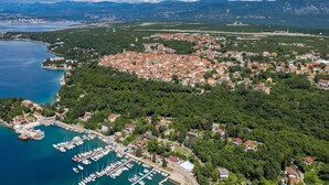 An aerial view of a coastal town with a marina, dense residential area, and surrounding mountains.