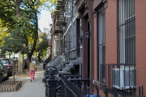 A row of townhouses with a fire escape, a sidewalk, and parked cars.