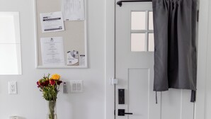 A room with a wooden table, a vase with flowers, a bulletin board with papers, a white door with a curtain, and a light switch. - Manhattan Bridge-Brooklyn-UN (Brooklyn)