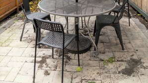 A round metal table with four chairs, a striped umbrella, and a wooden fence in the background. - Manhattan Bridge-Brooklyn-UN (Brooklyn)